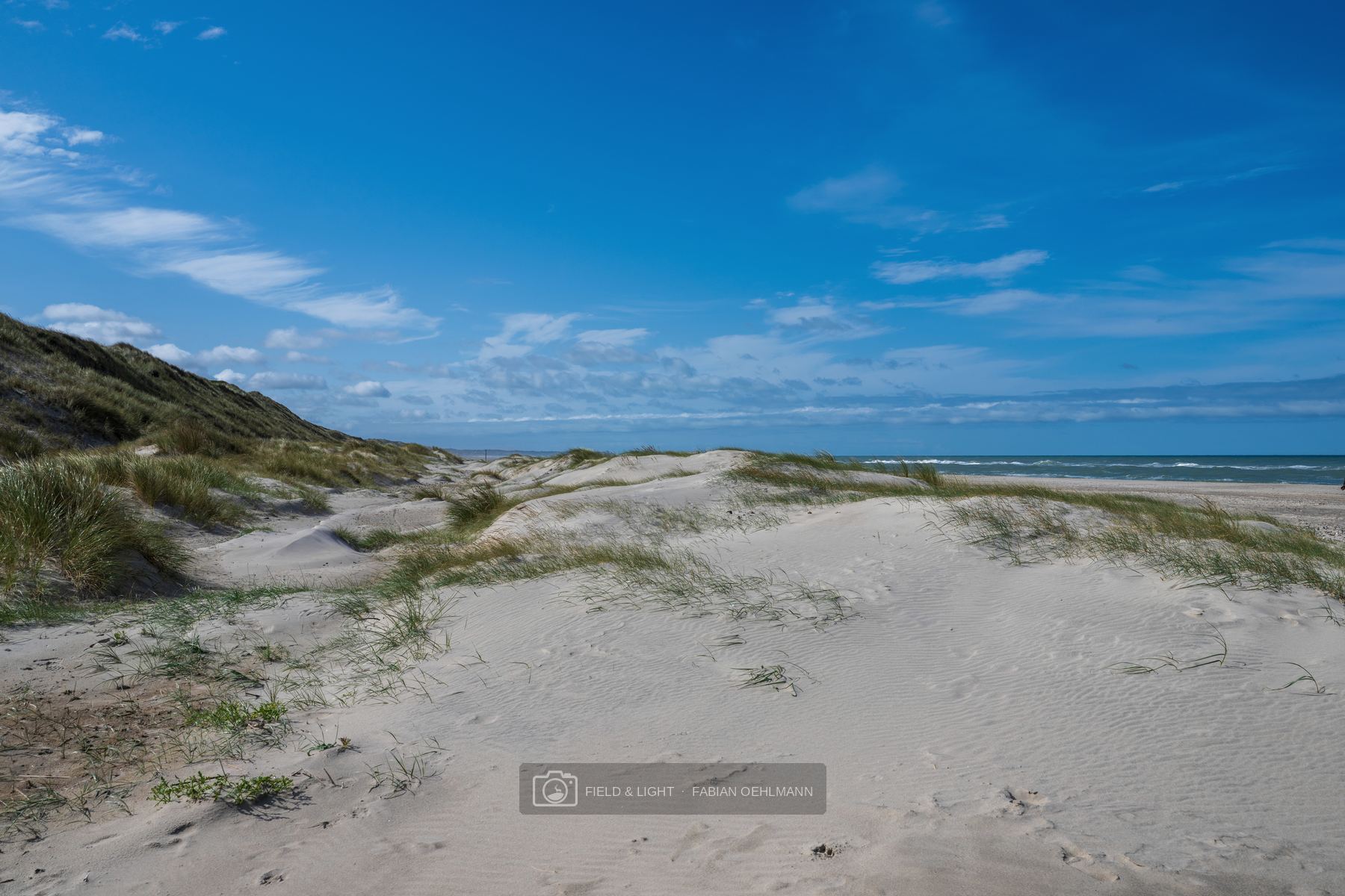 Layered white dunes opening towards the blue North Sea beneath a clear summer sky