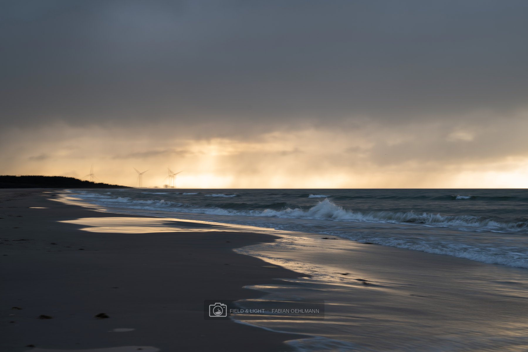 A curving North Sea shoreline reflecting the last light beneath a dark cloud bank