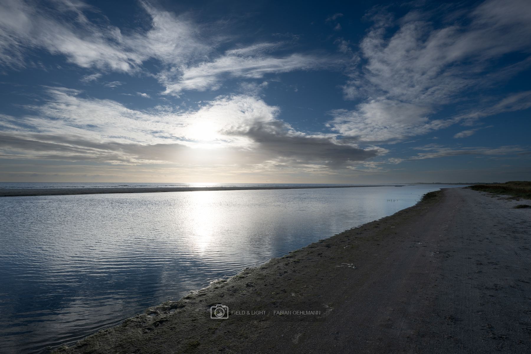 A tidal channel reflecting the low morning sun beside a curving beach at Jerup